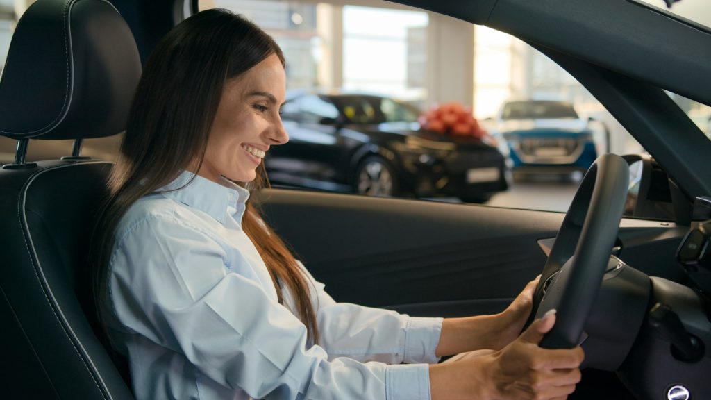 Happy Caucasian successful businesswoman joyful woman sit in new car in automobile shop rent service